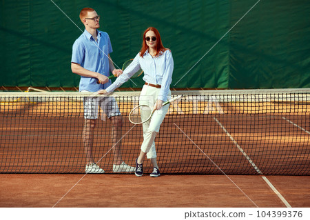 Beautiful young redhead woman and handsome man in stylish casual clothes and trendy eyewear accessories posing on tennis court Beautiful young redhead woman and handsome man in stylish casual clothes and trendy eyewear accessories posing on tennis court 104399376