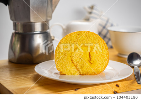 Side view coffee time with delicious homemade cake roll filled with pineapple jam in white ceramic plate. Side view coffee time with delicious homemade cake roll filled with pineapple jam in white ceramic plate. 104403180