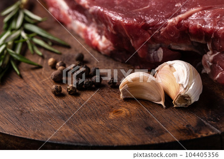 Raw steak on wooden cutting board with garlic, pepper and rosemary. 104405356