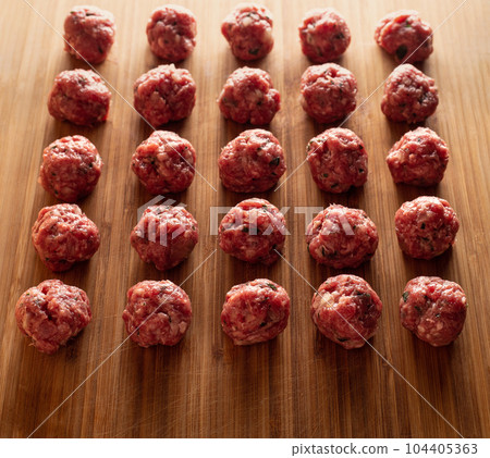 Raw uncooked meatballs on wooden cutting board. 104405363