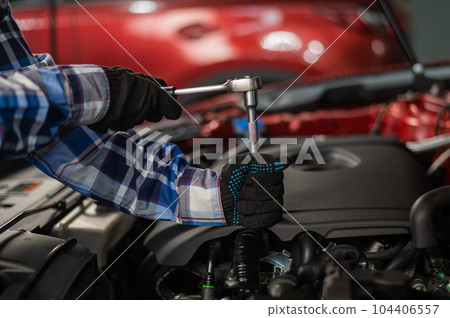 Female auto mechanic unscrewing a nut to replace a car spark plug. 104406557