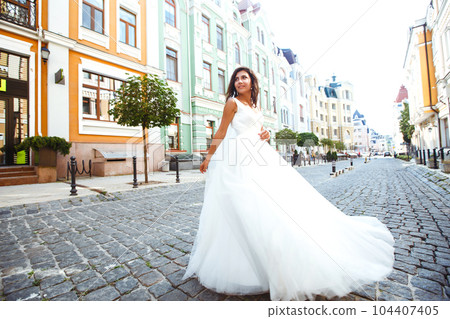 Young elegant bride in a white dress in the city. Beautyful bride with luxury make-up and hairstyle. 104407405