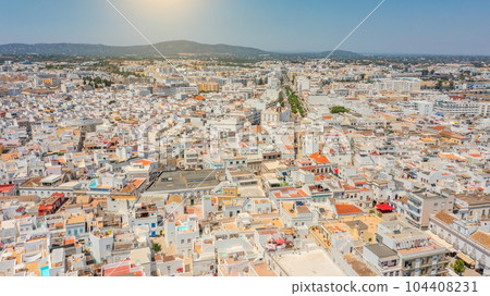 Aerial view of Portuguese fishing tourist town of Olhao with a view the mountain Cerro de Sao Miguel. sun in the background 104408231