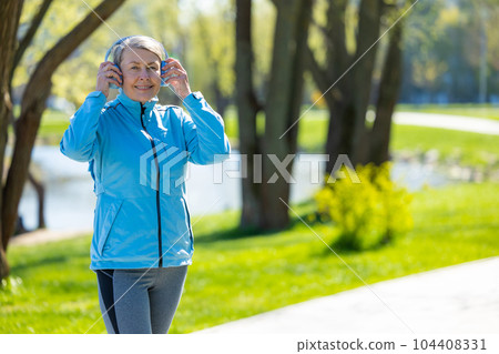 Woman in blue blazer in headphones in the park 104408331