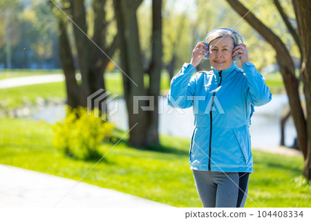 Woman in blue blazer in headphones in the park 104408334