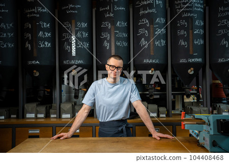 Entrepreneur wearing apron and glasses standing near counter of his cafe with big variety of coffee. 104408468