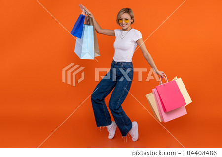 Delighted woman in white t shirt and jeans enjoying shopping jumping with bags Delighted woman in white t shirt and jeans enjoying shopping jumping with bags 104408486