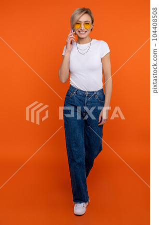 Confident woman in white t shirt and jeans talking on mobile phone pleasant conversation 104408508