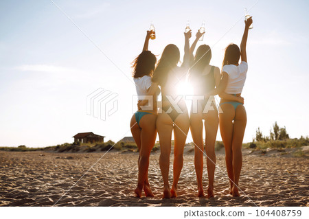 Four young girlfriends with beers in their hands raised together enjoying a holiday on the sea shore. 104408759