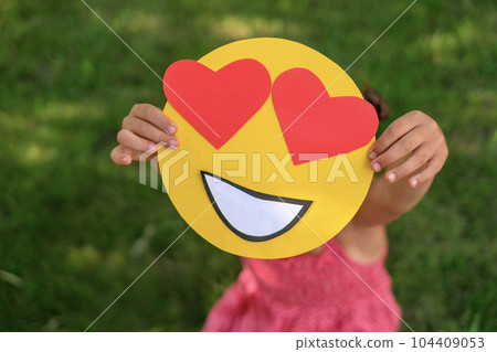 A close-up of the face of a lover smile with eyes in the shape of red hearts in the hands of a person. A close-up of the face of a lover smile with eyes in the shape of red hearts in the hands of a person. 104409053