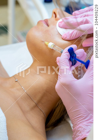 PRP ttherapy in beauty clinic, cosmetologist doing injections to woman's face to cure problem skin. 104409229