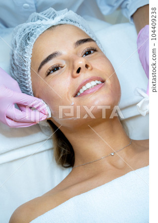 Beautician's hands cleaning female face with cotton pads at aesthetic clinic. 104409238