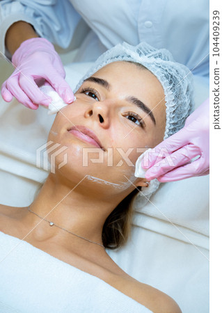 Beautician doctor cleaning woman face with cotton pads, skin care procedures, rejuvenation. 104409239