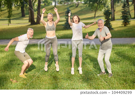 Group of healthy runners team jumping in the air at city park during morning training. 104409299