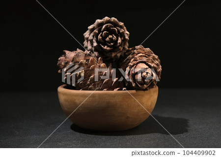 a cedar cone in a wooden bowl on a black a cedar cone in a wooden bowl on a black 104409902