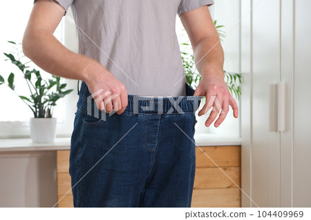 The guy is trying on big jeans after losing weight The guy is trying on big jeans after losing weight 104409969