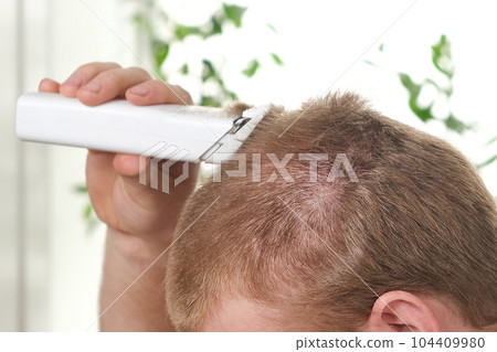 A man cuts his hair with a clipper. Haircut at 104409980