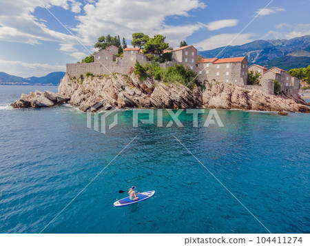 Young women Having Fun Stand Up Paddling in blue water sea near st stefan island in Montenegro. SUP Young women Having Fun Stand Up Paddling in blue water sea near st stefan island in Montenegro. SUP 104411274