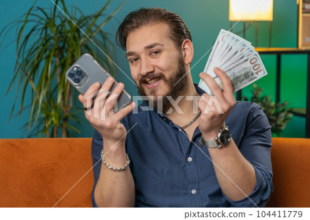 Smiling happy lebanese man counting money cash use smartphone, income saves lottery win budget 104411779