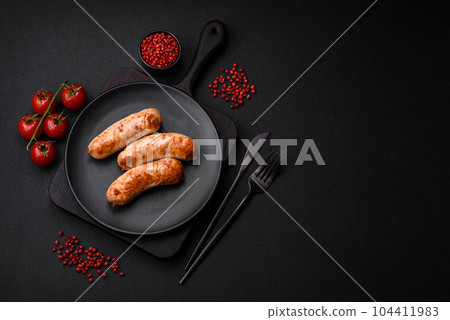 Delicious juicy grilled sausages with salt, spices and herbs on a ceramic plate 104411983