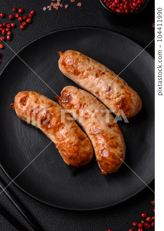 Delicious juicy grilled sausages with salt, spices and herbs on a ceramic plate 104411990