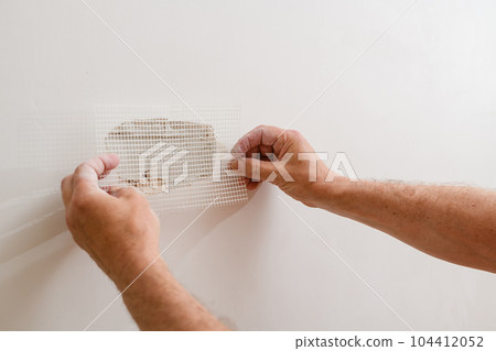 A handyman is repairing a hole in the drywall in the wall. A handyman is repairing a hole in the drywall in the wall. 104412052