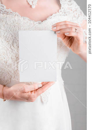 Woman wearing a wedding dress holding wedding stagionery invitation card mockup 5x7 on white wall background 104412570