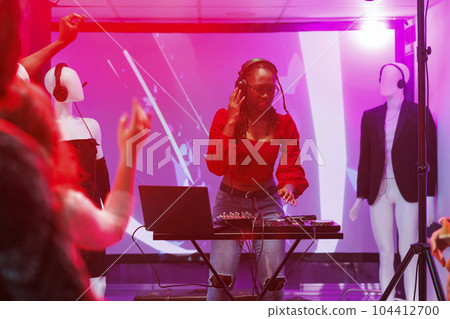 Woman dj mixing electronic music using digital controller in nightclub. African american musician in headphones performing on stage with sound mixer console at club party Woman dj mixing electronic music using digital controller in nightclub. African american musician in headphones performing on stage with sound mixer console at club party 104412700