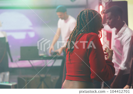 Young cheerful african american woman laughing while partying in crowded nightclub. Happy smiling girl having fun and enjoying nightlife at discotheque party in club at night Young cheerful african american woman laughing while partying in crowded nightclub. Happy smiling girl having fun and enjoying nightlife at discotheque party in club at night 104412701