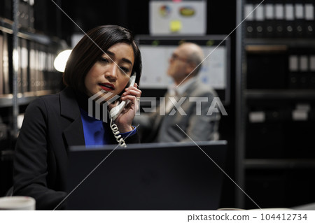 Bookkeeping businesswoman offering consultancy during phone call in administrative workplace. Asian employee in archival depository filled with document folders and flowcharts 104412734