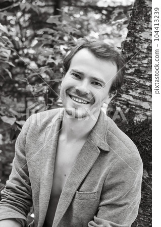 Black and white portrait of Self assured smiling young handsome man with naked chest and open grey jacket. Macho with dark hair, sideburns and beard looking at camera. Black and white portrait of Self assured smiling young handsome man with naked chest and open grey jacket. Macho with dark hair, sideburns and beard looking at camera. 104413239