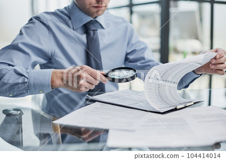 Businessman looking through a magnifying glass to documents 104414014