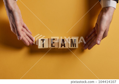 The word TEAM is written on wooden cubes on a black table surface. 104414107