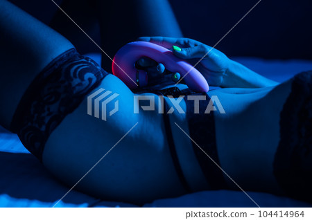A woman in black lace lingerie lies on a bed in the dark and holds a vibrator. A woman in black lace lingerie lies on a bed in the dark and holds a vibrator. 104414964