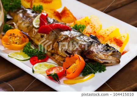 Baked whole trout with potatoes, greens and tomatoes on plate, glass of wine 104415010