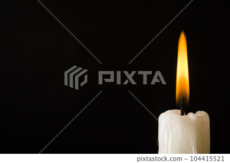White candle burning with yellow fire on a black background 104415521