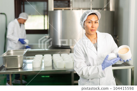 Woman in white uniform working in shaping workshop of cheese dairy 104415598