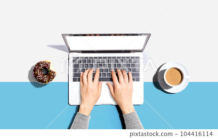 Person using a laptop computer with a donut and a cup of coffee 104416114