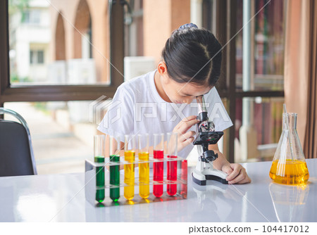 little scientist looking through a microscope and test tubes filled with chemicals for learning about science and experiments. little scientist looking through a microscope and test tubes filled with chemicals for learning about science and experiments. 104417012