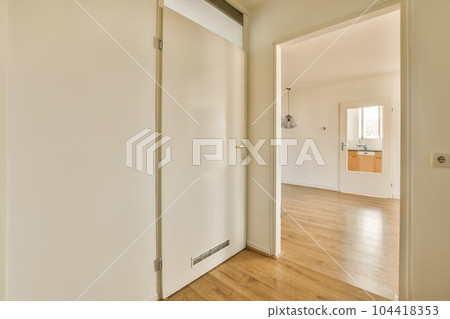 an empty room with wooden floors and white walls, there is a door leading to the hallway that leads to another room an empty room with wooden floors and white walls, there is a door leading to the hallway that leads to another room 104418353
