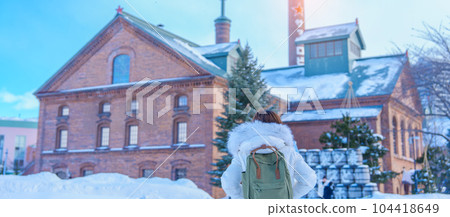 Woman tourist Visiting in Sapporo, Traveler in Sweater looking Sapporo Beer Museum with Snow in winter season. landmark and popular for attractions in Hokkaido, Japan. Travel and Vacation concept 104418649