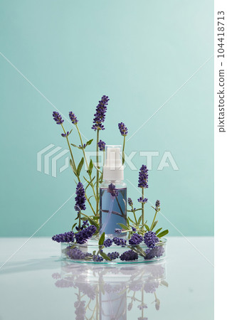 Color liquid is contained inside a pump bottle standing on round podium, lavender flowers decorated around. Container packaging of Lavender (Lavandula) extract 104418713