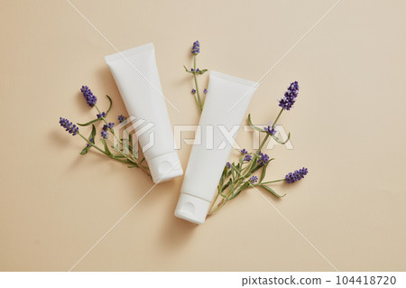 Over beige background, two white tubes are displayed with lavender flower. Mockup of skin care cosmetic tube of beauty facial extracted from Lavender (Lavandula) Over beige background, two white tubes are displayed with lavender flower. Mockup of skin care cosmetic tube of beauty facial extracted from Lavender (Lavandula) 104418720