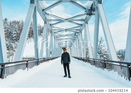 man tourist Visiting in Biei, Traveler in Sweater sightseeing Shirahige Waterfall bridge with Snow in winter. landmark and popular for attractions in Hokkaido, Japan. Travel and Vacation concept man tourist Visiting in Biei, Traveler in Sweater sightseeing Shirahige Waterfall bridge with Snow in winter. landmark and popular for attractions in Hokkaido, Japan. Travel and Vacation concept 104419214
