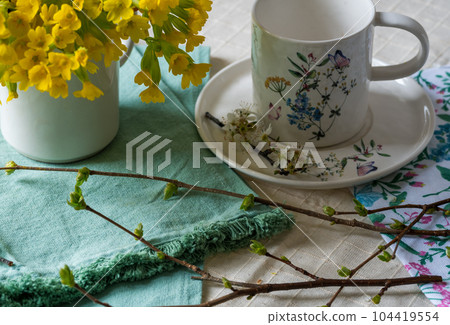 Spring still life with yellow primroses, an apple branch and a cup 104419554