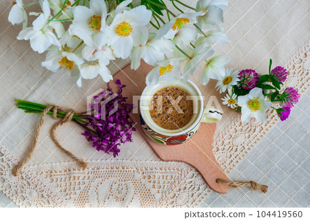 Coffee with foam and spring wildflowers on a white tablecloth. Coffee with foam and spring wildflowers on a white tablecloth. 104419560