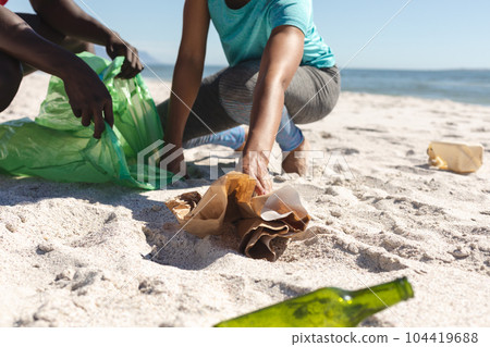 Low section of african american couple cleaning sunny beach and collecting litter Low section of african american couple cleaning sunny beach and collecting litter 104419688