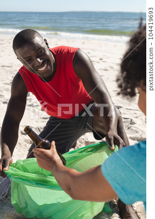 Happy african american couple cleaning sunny beach and collecting litter 104419693