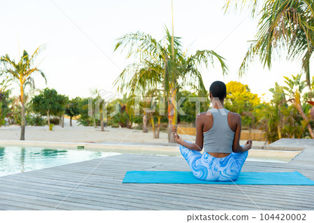 Rear view african american woman practicing yoga meditation sitting on beach deck, copy space Rear view african american woman practicing yoga meditation sitting on beach deck, copy space 104420002