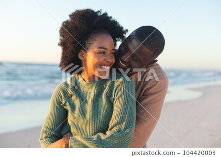 Happy african american couple embracing and smiling on sunny beach Happy african american couple embracing and smiling on sunny beach 104420003